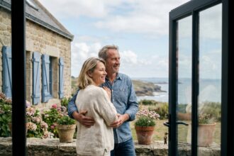 Couple heureux sur terrasse en pierre d'une maison familiale bretonne avec vue sur la côte atlantique et fleurs sauvages