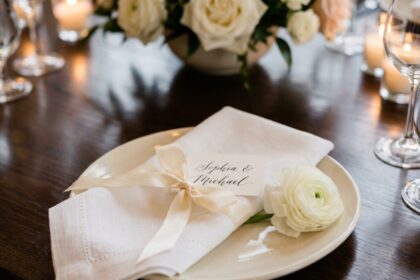 Gros plan détaillé des détails de mariage sur table, serviette blanche avec nœud ruban, marque-place calligraphié et fleur blanche délicate