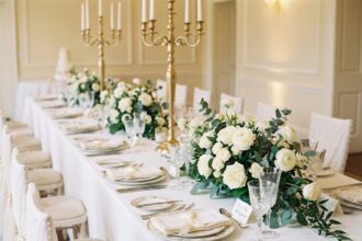 table de mariage élégante avec nappe blanche, bougies dorées et centre de table en roses blanches et eucalyptus