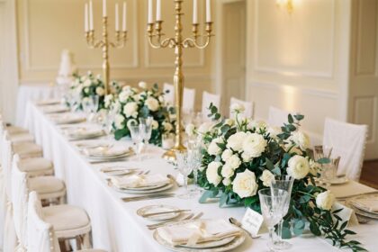 table de mariage élégante avec nappe blanche, bougies dorées et centre de table en roses blanches et eucalyptus