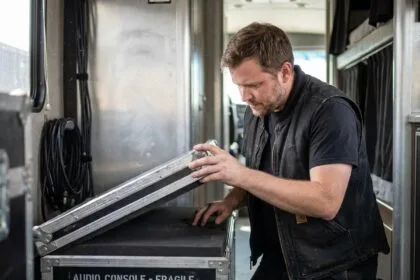 Technicien route inspectant l'intérieur d'un flight case d'occasion contenant du matériel audio professionnel en tournée