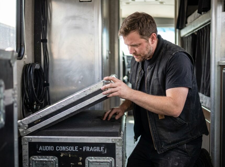 Technicien route inspectant l'intérieur d'un flight case d'occasion contenant du matériel audio professionnel en tournée